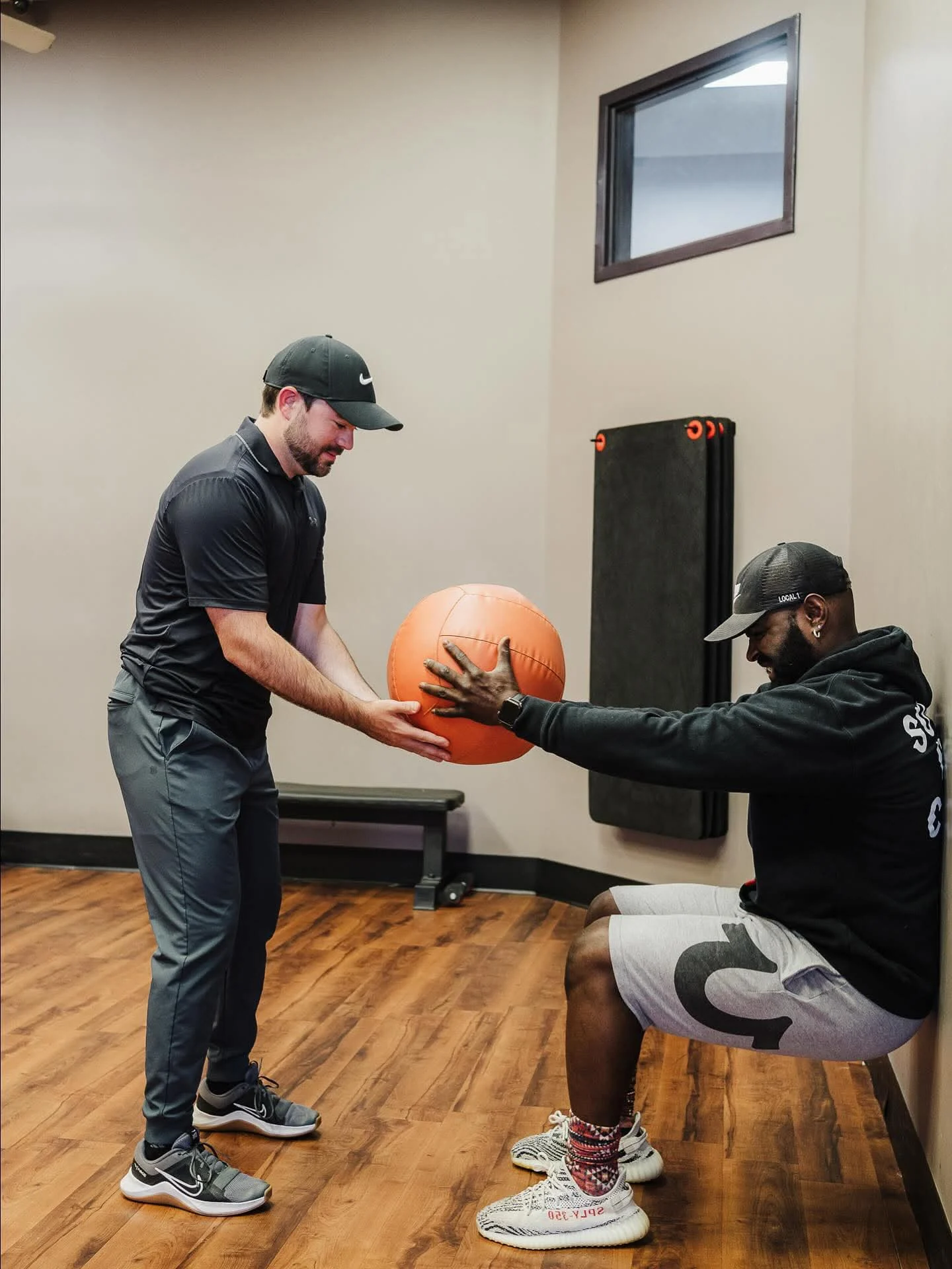 Trainer coaching a member through a wall-sit with a medicine ball at E’ville Fitness